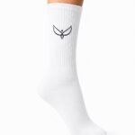 White knee-high sock on a leg with a small black bird logo on the shin area, ribbed texture visible against a white background